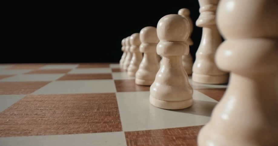Lightcolored chess pieces aligned on a checkered board against a dark background