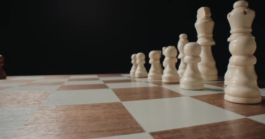 Chess pieces stand in their starting positions on a chessboard in a dark area