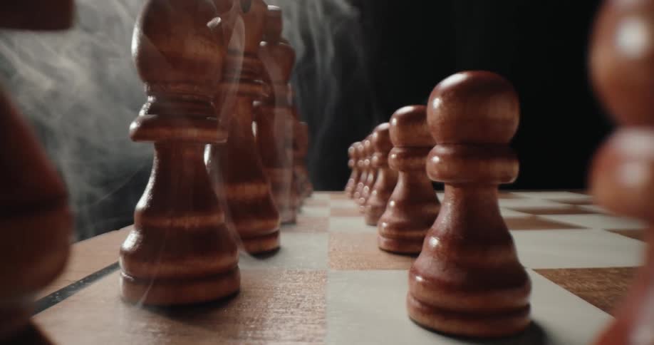 Wooden chess pieces lined up on a checkered board in a dark setting
