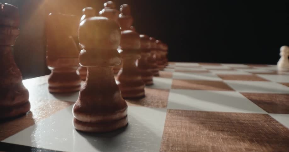 Closeup of wooden chess pieces arranged on a board with moody lighting