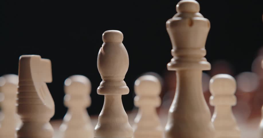 The camera pans across a wooden chessboard shifting focus from a queen piece to a bishop and knight while keeping the background pieces in a soft blur against a dark backdrop