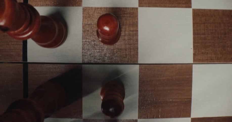 A hand reaches into the frame to move a dark wooden pawn across a checkered chessboardthe topdown perspective captures the strategic movement among other stationary chess pieces during the game