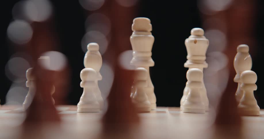 White chess pieces stand on a wooden board while the camera pans across the set revealing the king queen and pawns against a dark background with soft bokeh lights