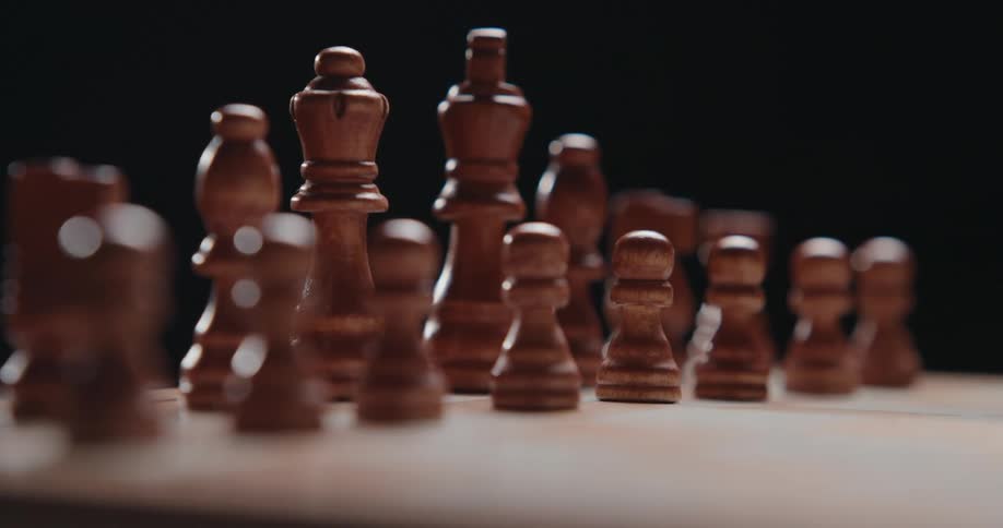 Close up of brown chess pieces arranged on a side of a chess board in a dark room