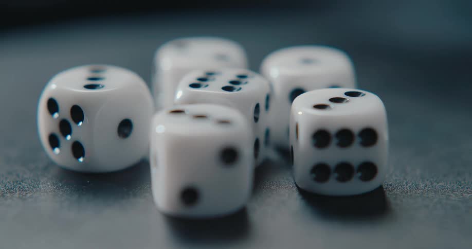A close view of several white dice with black pips resting on a dark surface as the camera slowly pans around them