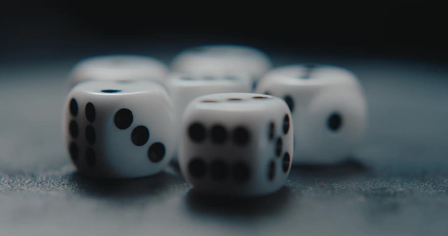 Several white dice with black pips across a dark textured surface in a closeup shot that uses a shallow depth of field to highlight their movement against a blurred background