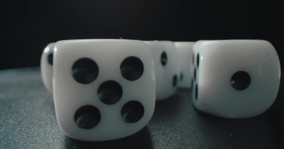 A closeup video shows several white dice with black pips across a dark flat surface under a bright light