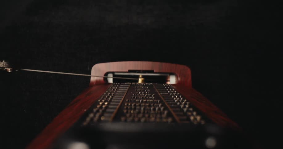 A high angle view looks down the wooden face of a mechanical metronome showing its metal pendulum swinging rapidly back and forth against a solid black background