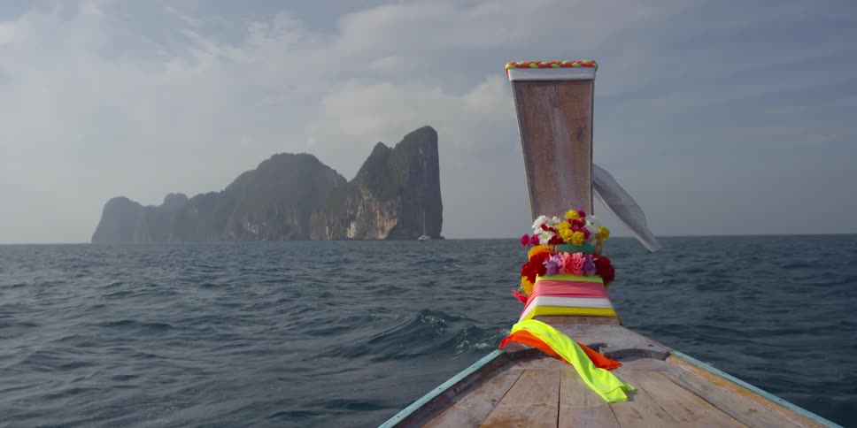 A boat with flowers and ribbons on it sailing through the ocean toward a large rock