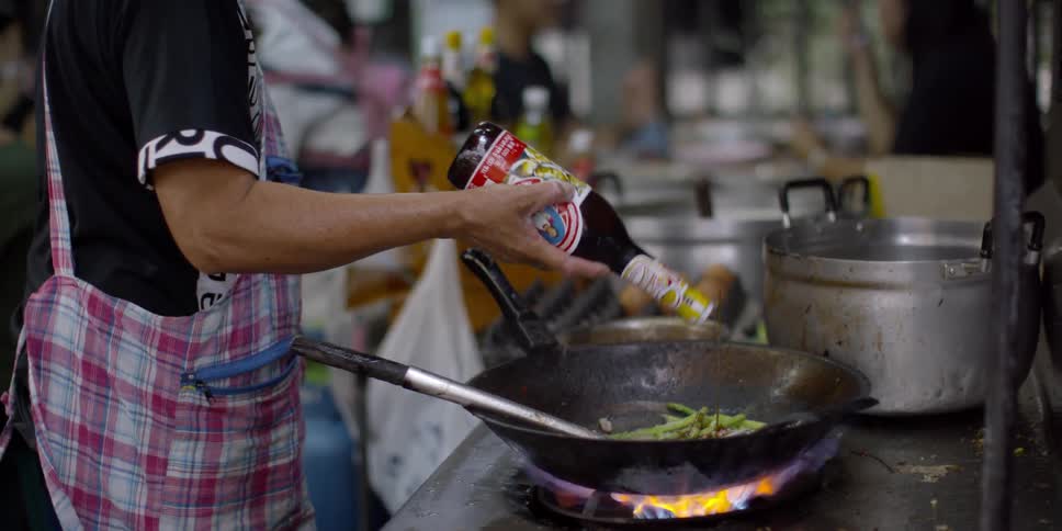 A chief puts soy sauce in a wok