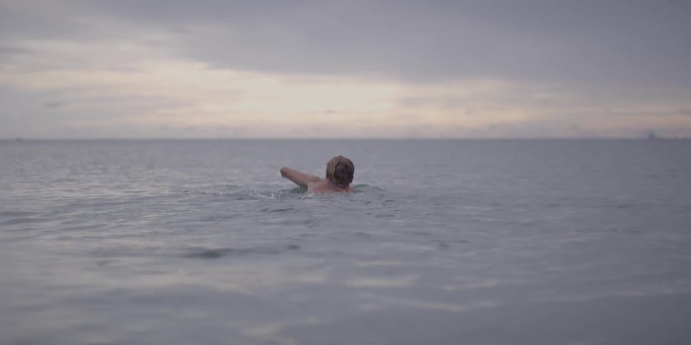 Man is swimming out into the ocean after sunset