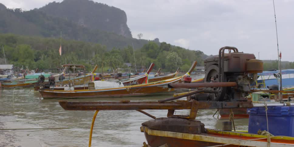 Boats sitting in the water by a mountain with clouds in the sky
