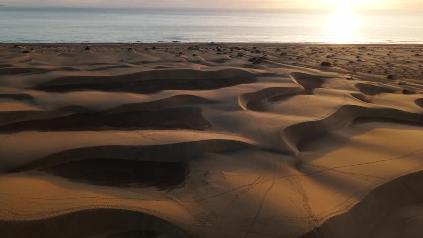 Aerial view of vast rolling sand dunes meeting the ocean coastline at golden sunset
