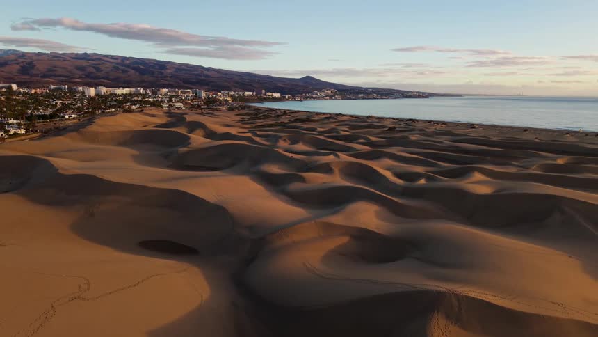 Coastal dunes extend toward the shoreline with a city and mountains in the background