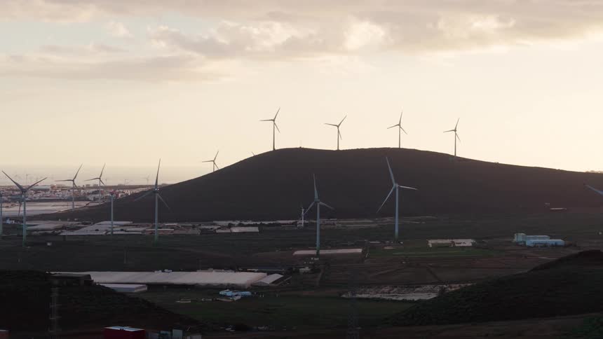 A windmill stands in the open countryside its blades rising above a wide rolling landscape under a sky filled with soft drifting clouds