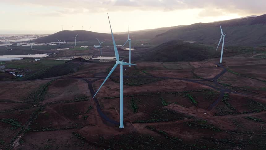 Wind turbines on a field with hills on the background outdoors during dusk or dawn