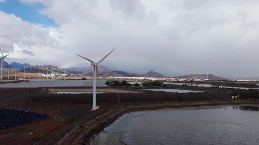 Wind turbines installed in a coastal area with a water reservoir and a city in the background