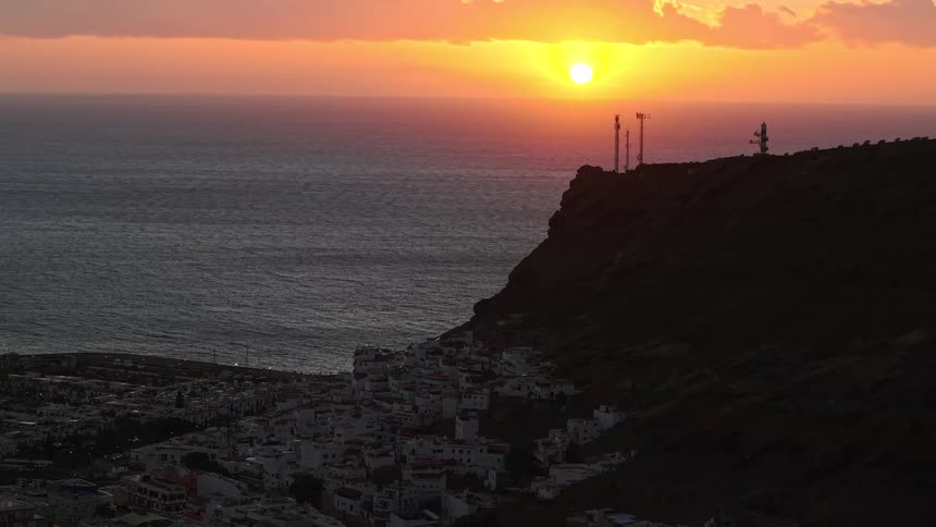 Soft golden sunset over a rugged coastline with a hillside village silhouetted above the sea