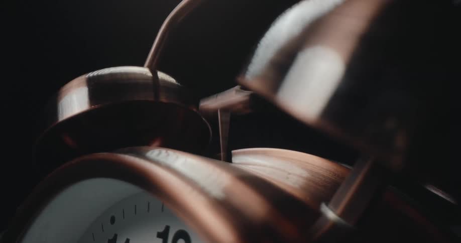 Metal alarm clock with twin bells appears in closeup against a dark background