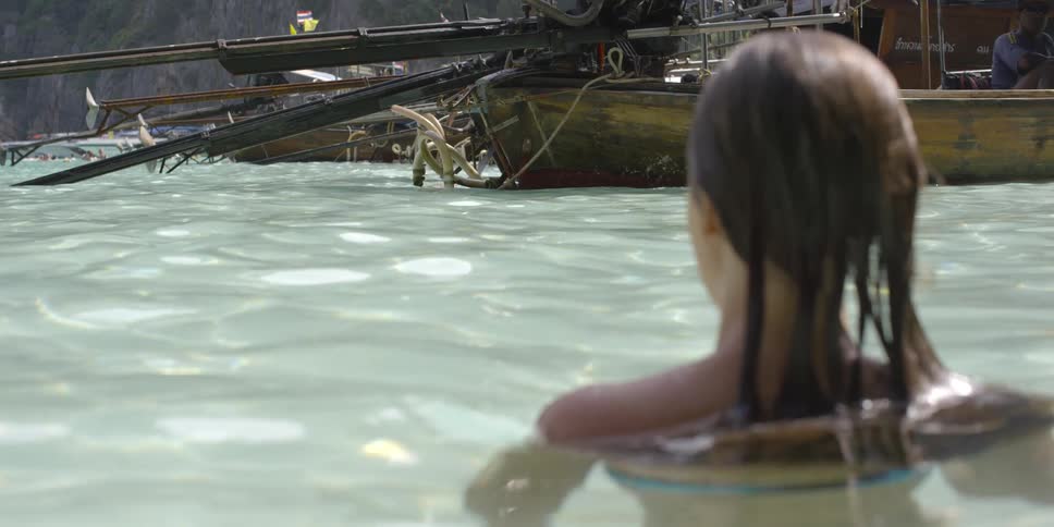 A woman is wading in neck deep water near fishing boats