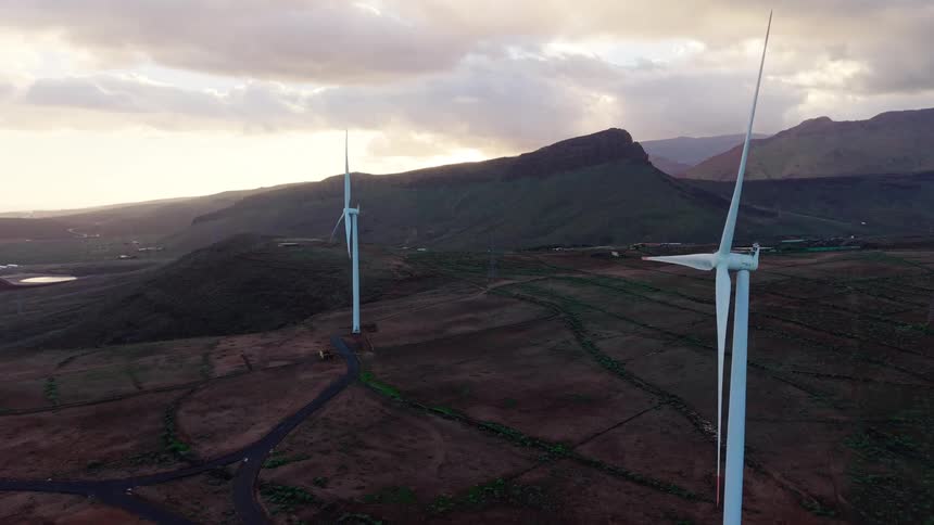 Natural landscape of mountains next to a field with wind turbines outdoors during dusk or dawn