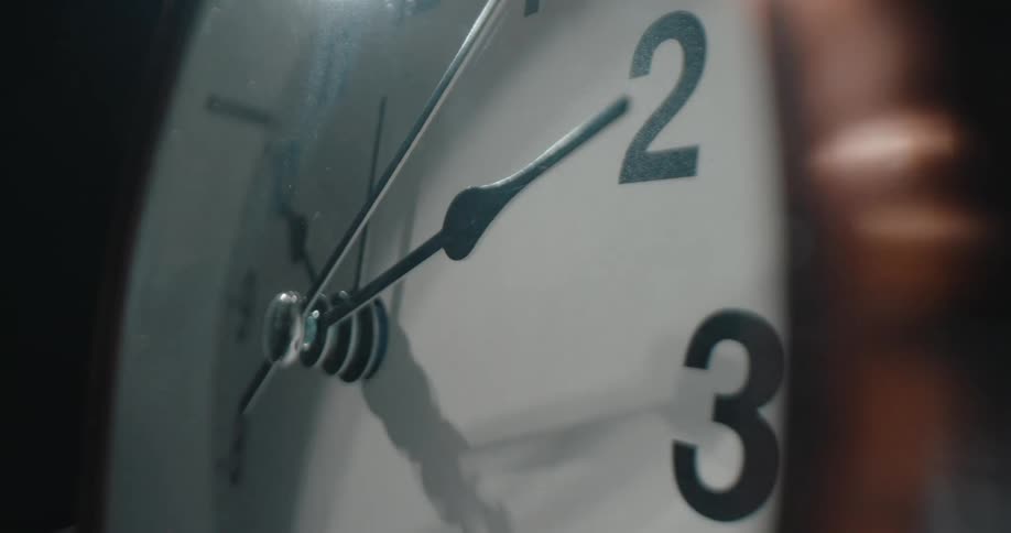 A closeup shot of an analog clock in an indoor setting passing the seconds while a indoor lighting brights the object