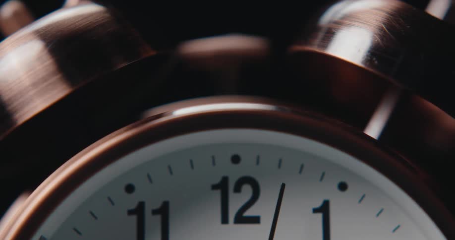 A closeup shot of a coppercolored vintage alarm clock with the bell ringing in an indoor setting with dark background