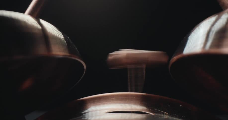 The central hammer moves rapidly back and forth in a horizontal line between two bellsthe curved edges of the metallic bells on either side create rounded vertical lines that frame the central motion
