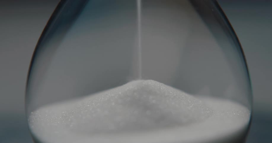 Sand flowing and accumulating at the base of a transparent glass hourglass