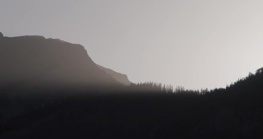 Mountain silhouette and tree line appear against a bright sky with a dark foreground area