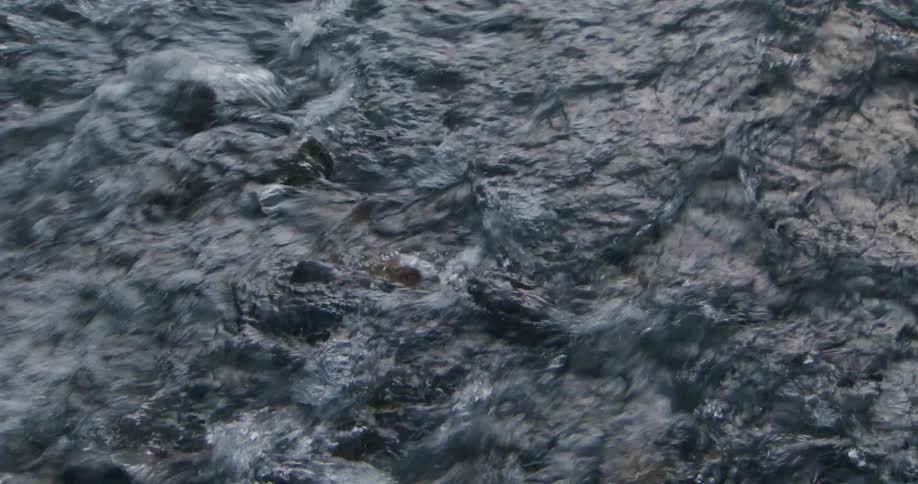 A closeup view of dark fastmoving water shows turbulent ripples and swirling currents with light reflecting off the uneven surface to emphasize the restless churning motion