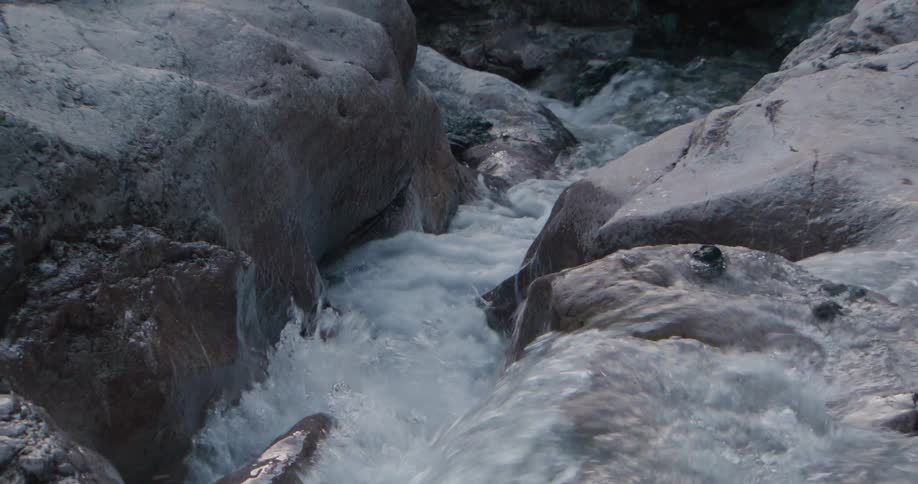 A close view shows water rushing between large grey rocks and flowing over a small ledge in a narrow stream