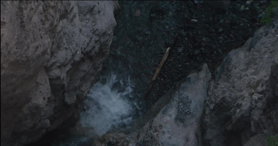 A narrow stream rushes through a rocky gorge white water churning between smooth gray stone walls as sparse greenery clings to the edges creating a secluded rugged scene shaped by erosion and natural flow