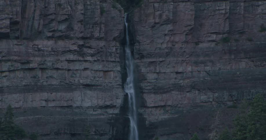 Waterfall descends through a crevice in a rocky cliff surrounded by forest