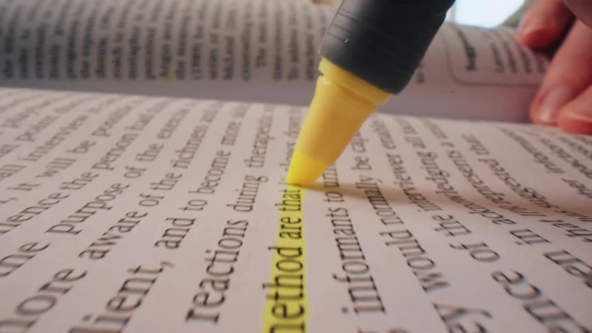 Person highlighting texts inside a textbook with a yellow marker