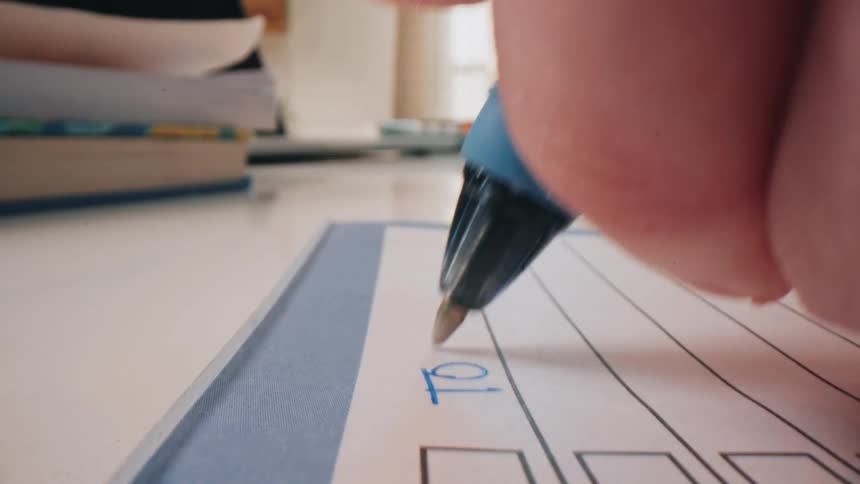 A person uses a blue ballpoint pen to write the words to do at the top of a lined paper document featuring several empty checkboxes on a white desk