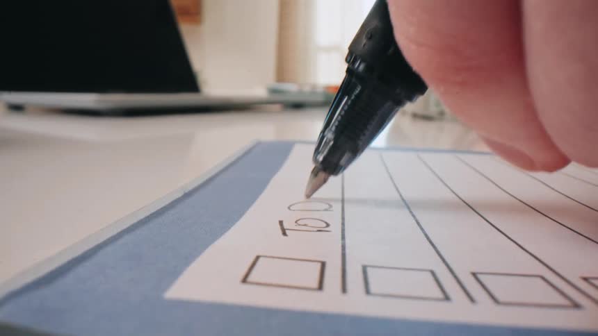 Person writes todo list with black pen in workspace setting