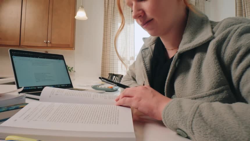 A focused young woman using laptop while studying at a kitchen counter