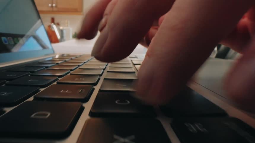 Hands typing on a laptop keyboard on a work desk with office items nearby