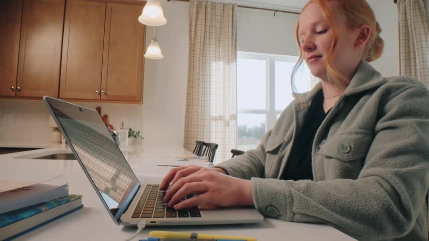 Young woman sitting at a desk typing on the keyboard of a laptop computer