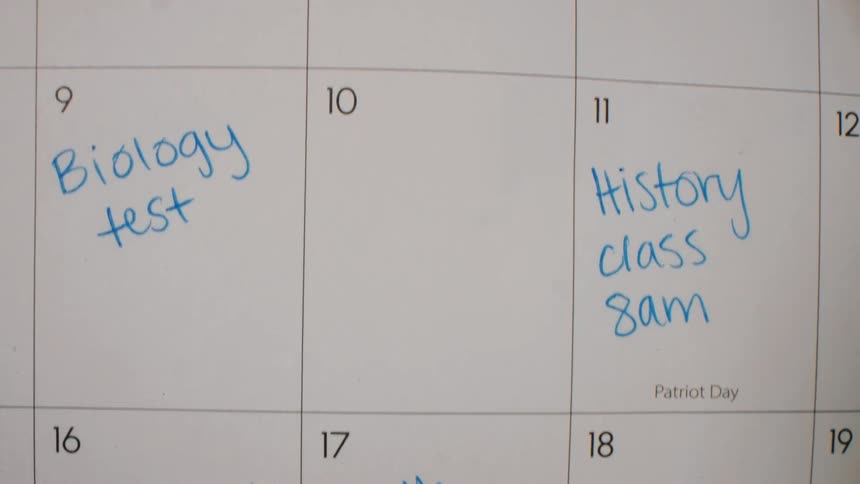 Paper monthly planner with numbered dates and blue handwritten notes indicating schoolrelated commitments