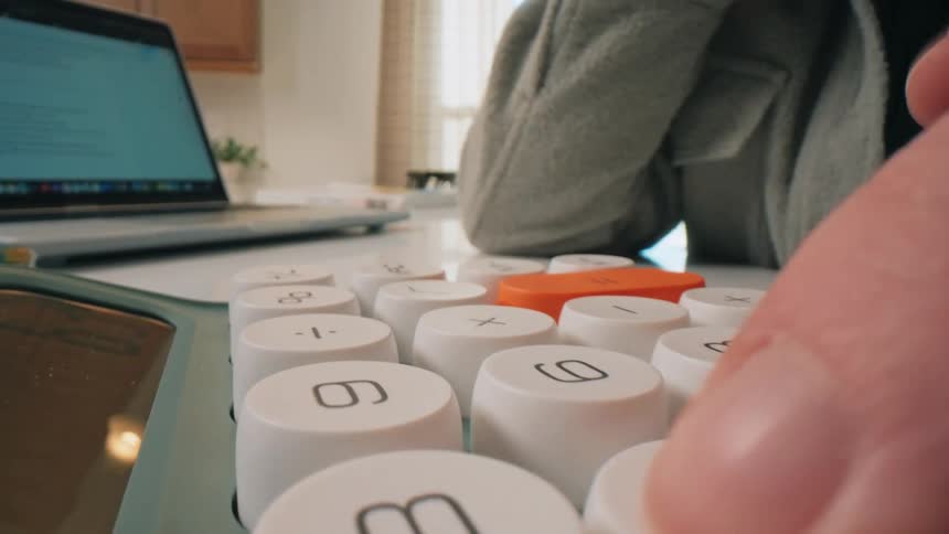 Person using largekey calculator next to laptop in indoor setting with furniture and plant