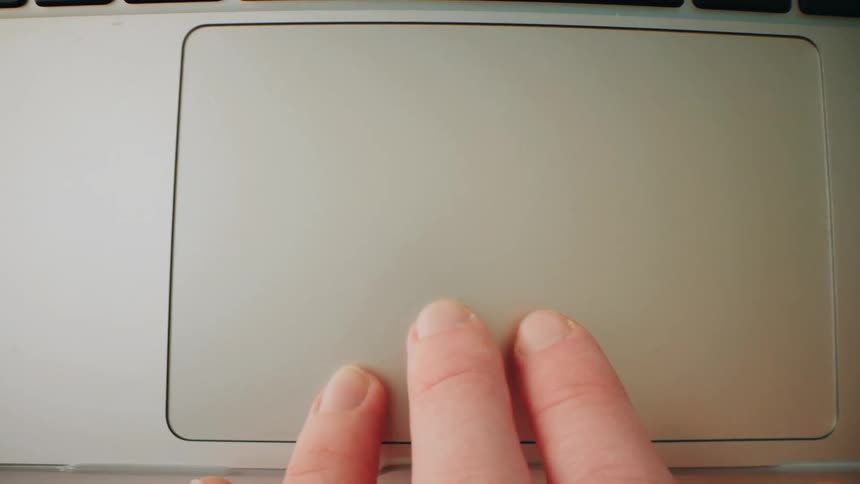 Human hand interacting with the touch pad of a laptop computer indoors