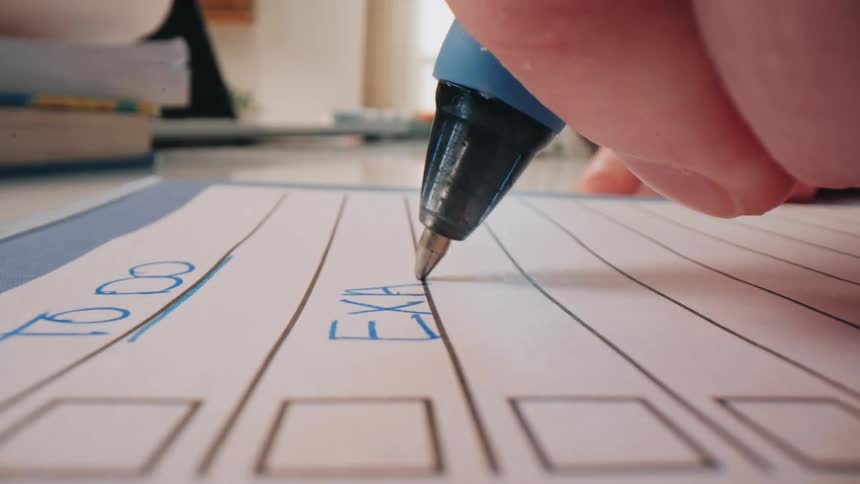 Hand writing in planner with books in study setting