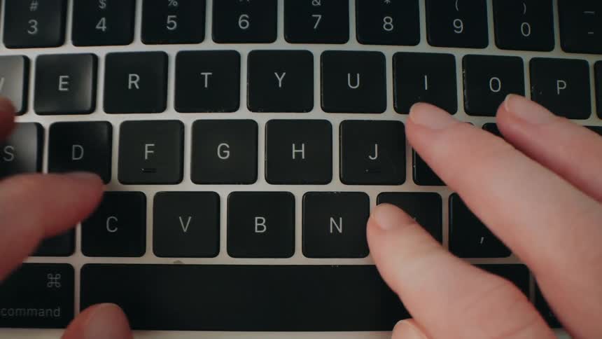 A persons hand types on a computer keyboard at midday bright natural light highlighting each keystroke as they work