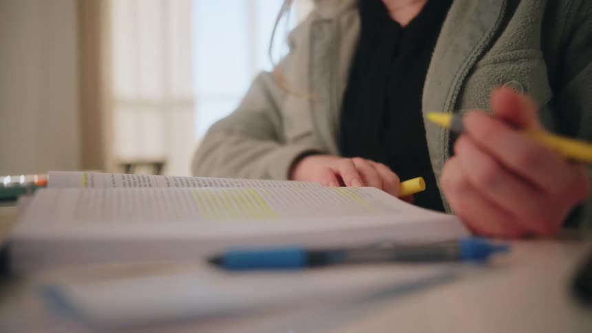 Person highlights book passages with yellow marker in study setting