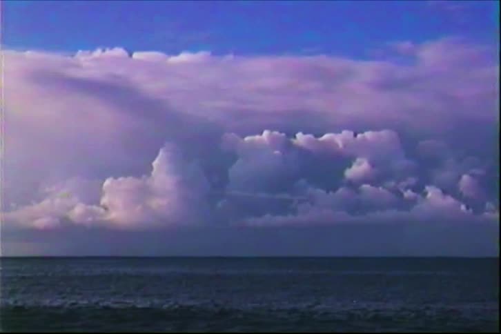 A wide archival shot captures dramatic clouds gathering over a dark ocean evoking a sense of calm and grandeur