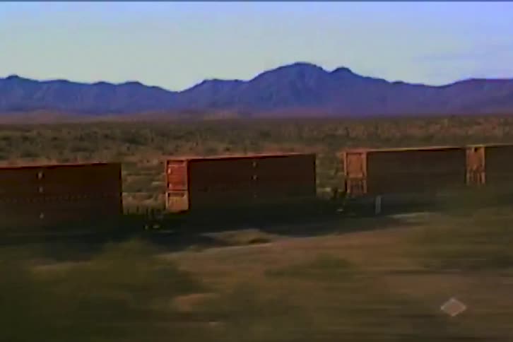 Freight train cars cross a desert landscape with mountains in the background
