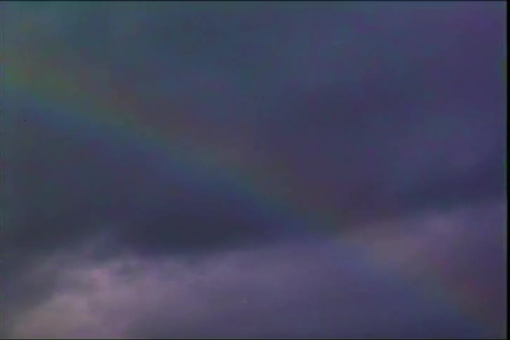 Rainbow appears over a dark mountain with cacti in the foreground under a cloudy sky