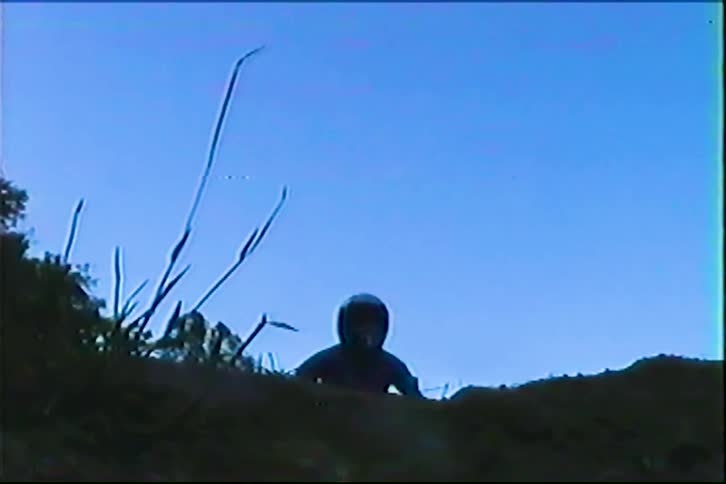 Motorcyclist on trail at dusk wearing helmet with silhouette outlined against dark blue sky